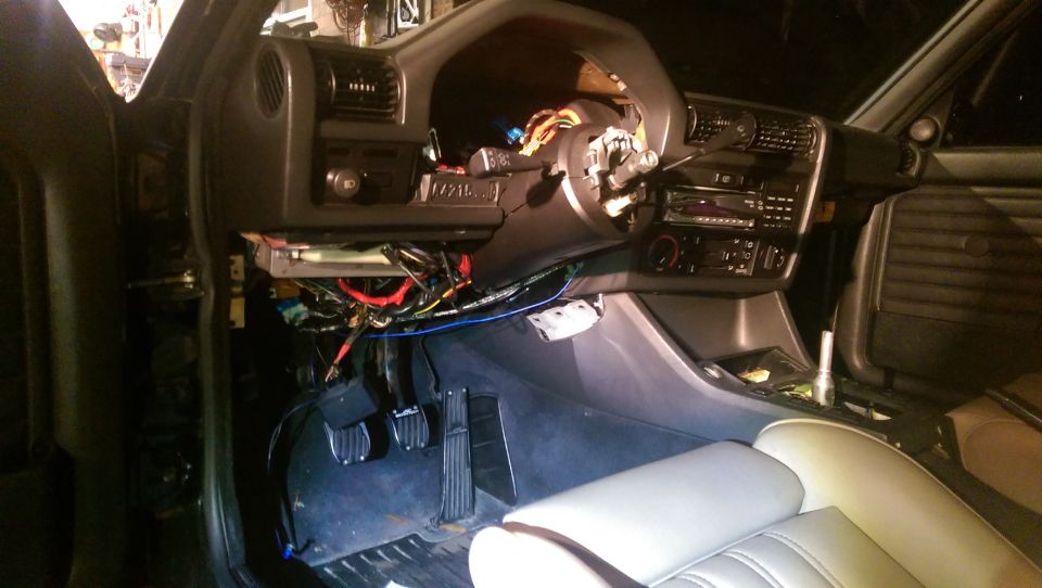 Car interior showing disassembled dashboard with wiring, steering column, and pedals.