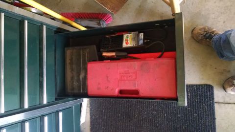 1994 Ford Bronco - A top-down view of an open toolbox drawer containing a red tool case, a battery tester, and jumper cables. The drawer is part of a dark gre…