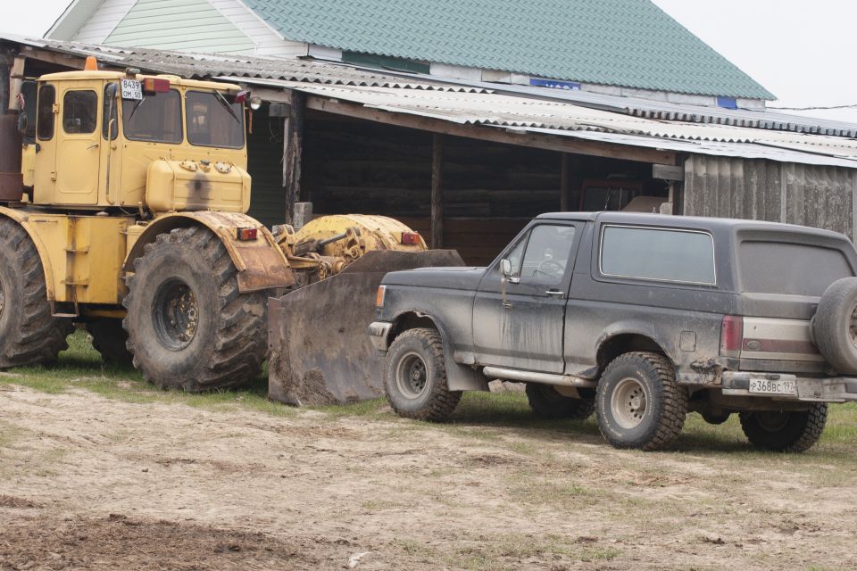Black Ford Bronco parked next to a yellow tractor.