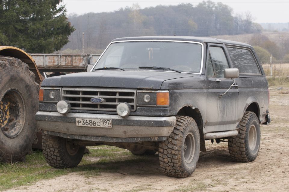 1987 Ford Bronco with off-road tires parked on dirt.