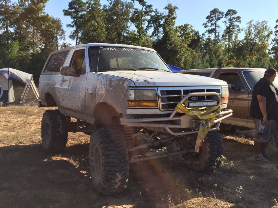Mud-covered white 1990s Ford Bronco with large tires and a light bar.