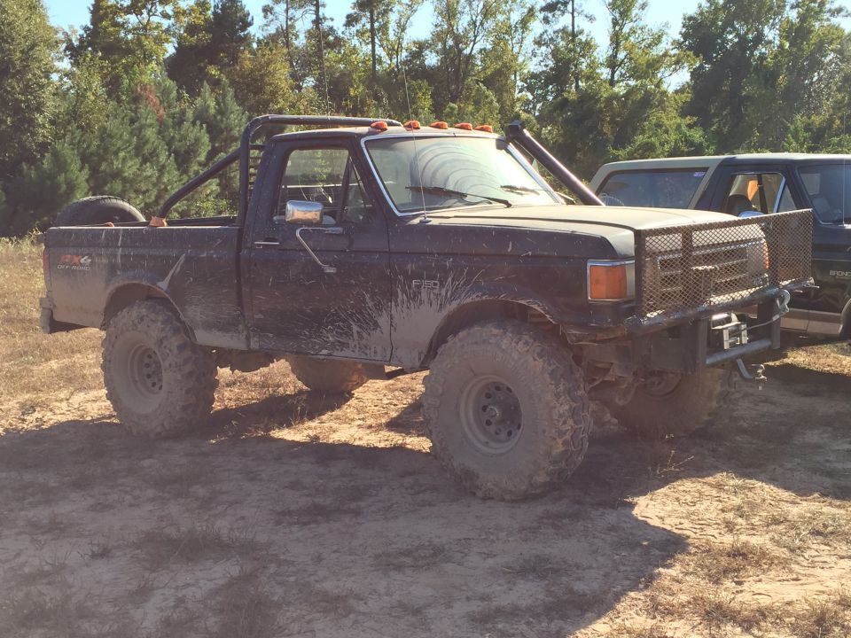 Muddy black Ford pickup truck with roll cage and large off-road tires.