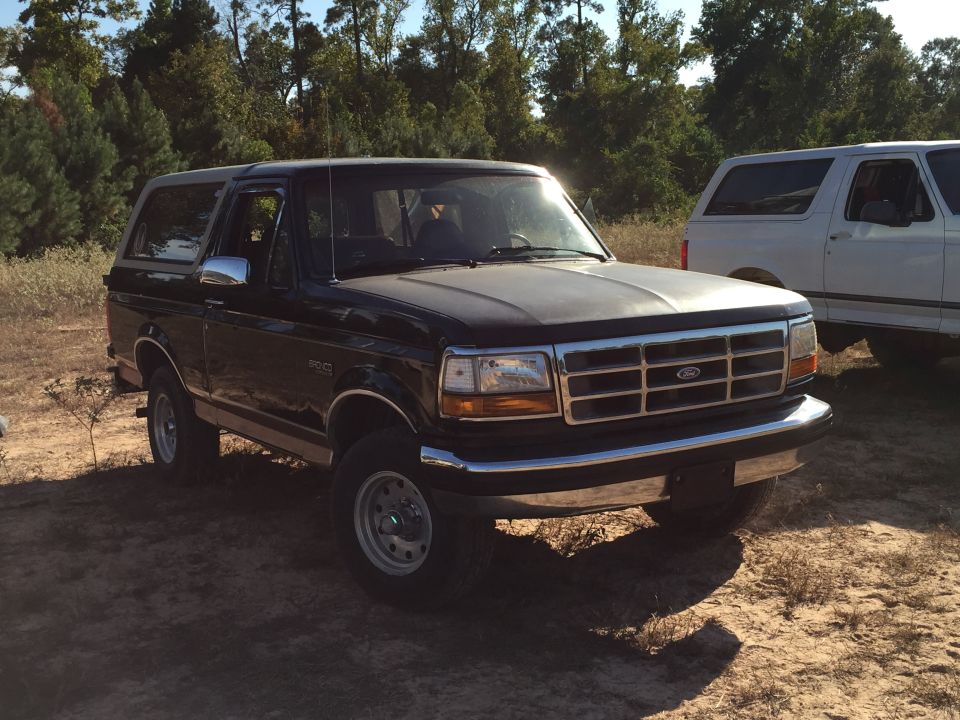 Black 1996 Ford Bronco parked on dirt lot with white Bronco behind it.