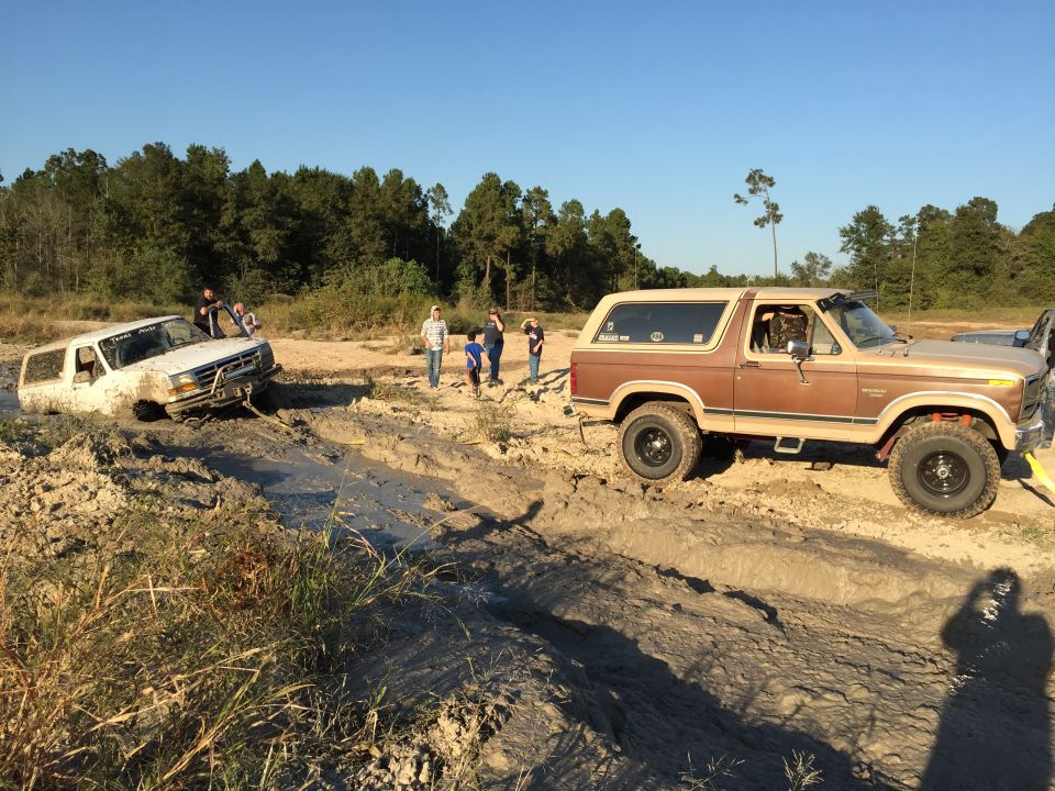 Two Ford Broncos stuck in mud, one being pulled out.