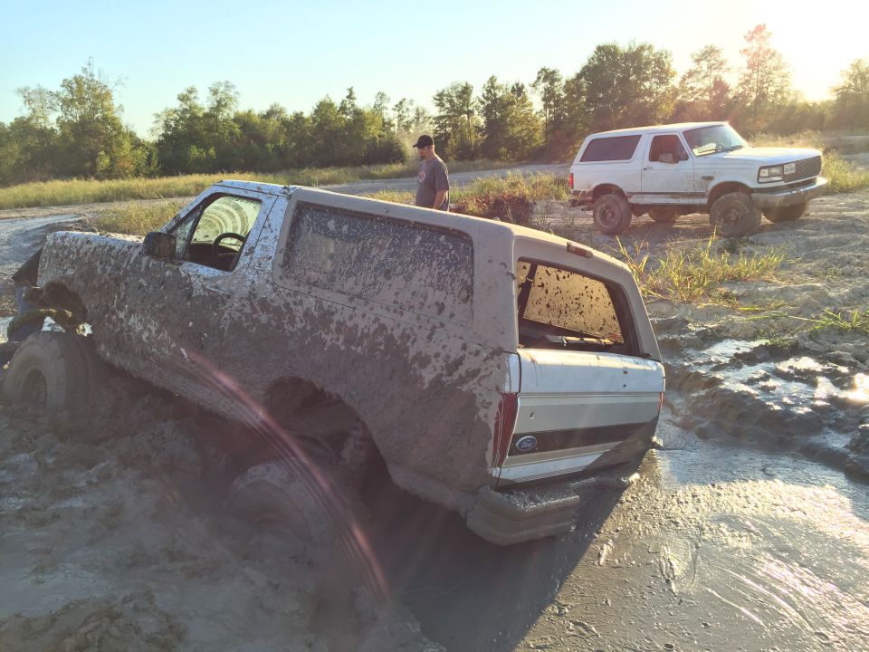 Mud-covered 1996 Ford Bronco stuck in mud, with a white Ford Bronco in the background.