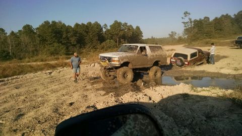 1996 Ford Bronco - A white Ford Bronco, covered in mud, is stuck in a muddy ditch next to a brown Ford Bronco that is also stuck. A man in a blue shirt and sh…