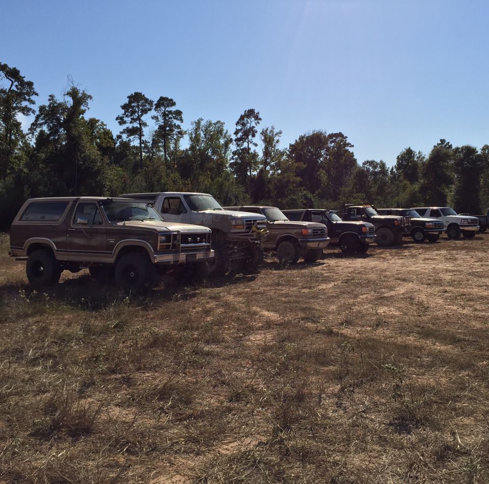 A line of modified trucks and SUVs parked in a dirt lot.