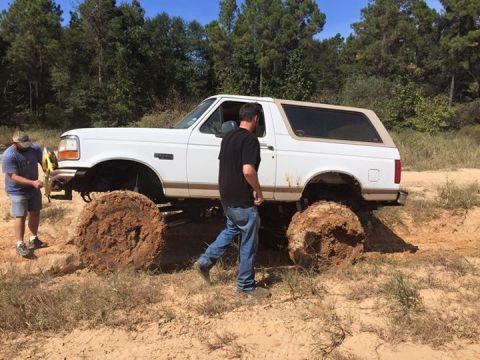 1996 Ford Bronco - A white Ford Bronco with large, mud-caked tires is stuck in the mud with two men standing nearby. The vehicle is lifted and appears to be o…