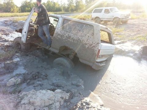 1996 Ford Bronco - A white Ford Bronco is stuck deep in mud with a person standing in the open driver's door. Another white Ford Bronco is visible in the back…