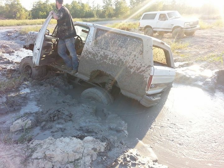 White Ford Bronco stuck in mud with driver's door open.