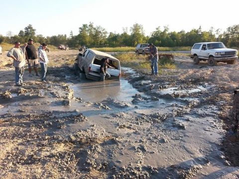 1996 Ford Bronco - A white Ford Bronco is stuck deep in mud with several people standing around it. Another white Ford Bronco is visible on the right side of…