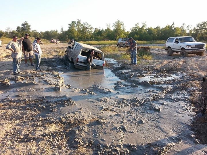 White Ford Bronco stuck in mud with people around; another Bronco visible.