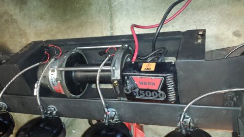 1996 Ford Bronco - A Warn 15000 winch is mounted on a black metal frame, with red and black power cables connected. Several black, round lights are attached t…