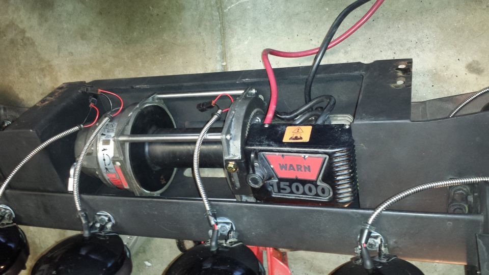 Warn 15000 winch on a black frame with power cables and lights.