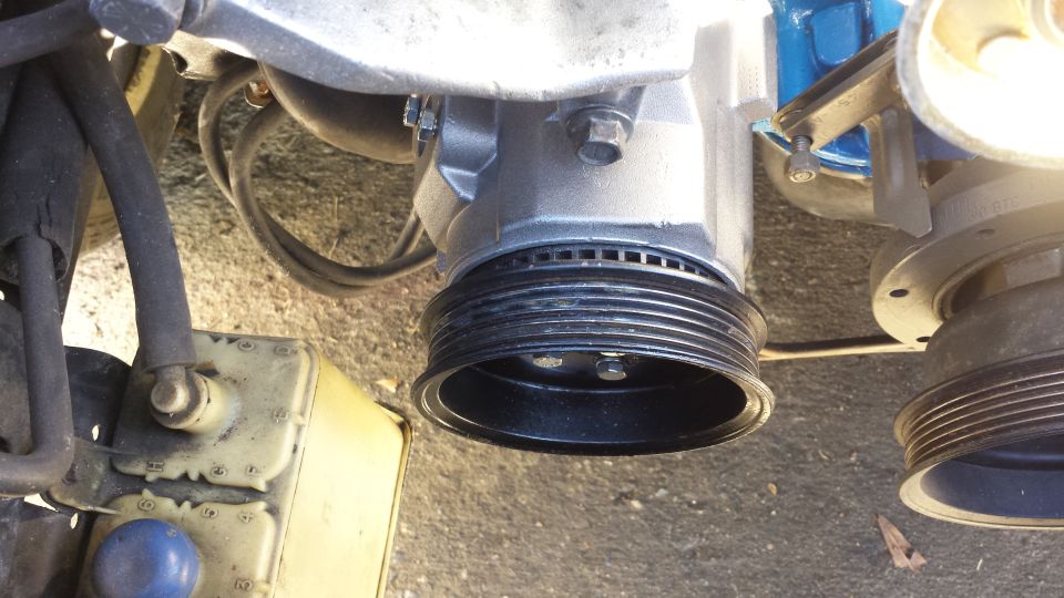 Close-up of vehicle engine pulleys and a yellow fluid reservoir.