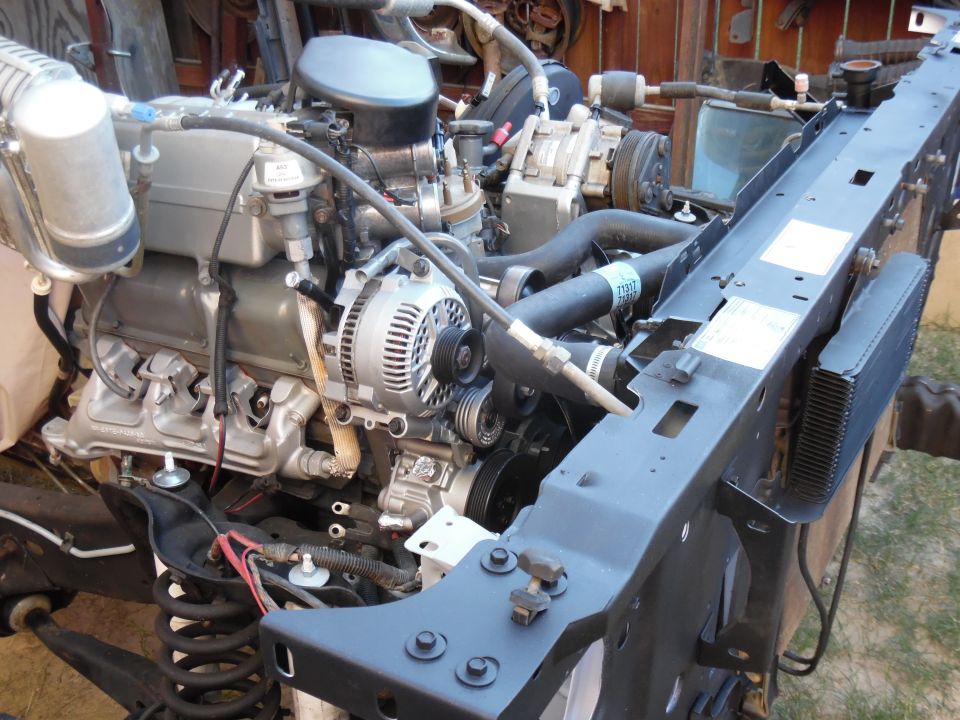 Silver V8 engine in stripped truck bay with black radiator support, alternator and A/C compressor