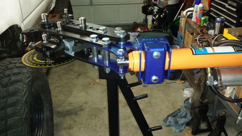 Hydraulic tube bender attached to vehicle frame near tire and degree gauge.