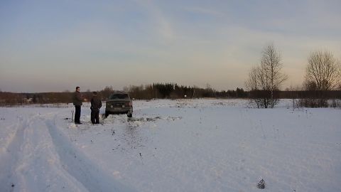 1987 Ford Bronco - Two men stand in a snowy field next to a dark-colored SUV that appears to be stuck in the snow. The vehicle is facing forward, and the surr…