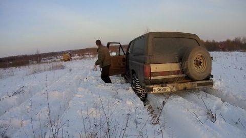 1987 Ford Bronco - A man exits a dark-colored SUV stuck in deep snow. The vehicle has a spare tire mounted on the rear and a license plate reading "P368BC 197…