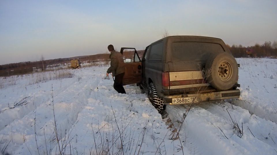 Man exiting a dark SUV stuck in snow, spare tire on back, license plate P368BC 197.