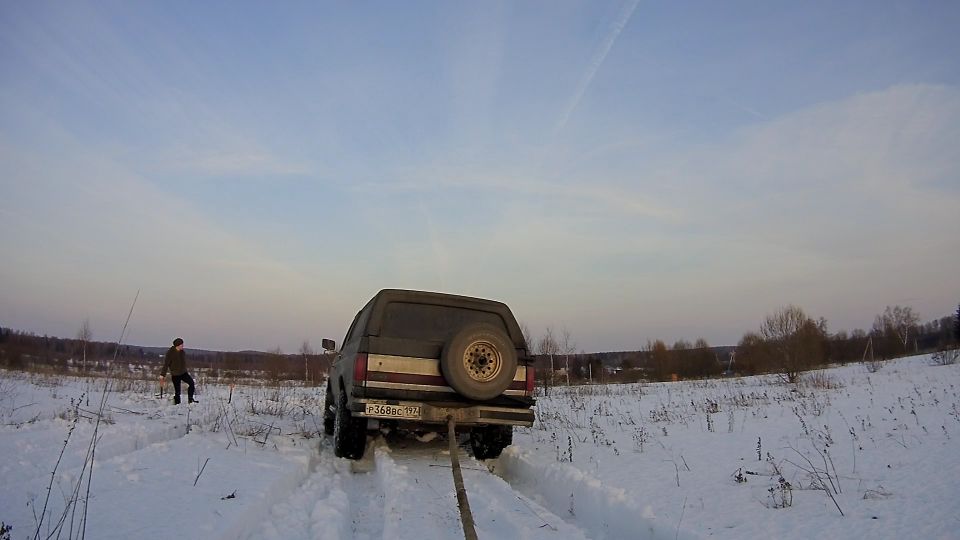 Rear view of a dark SUV stuck in snow with a tow rope attached.