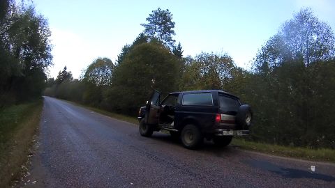 1987 Ford Bronco - A dark colored Ford Bronco is parked on the side of a wet, rural road with its driver's side door open. The vehicle is facing away from the…