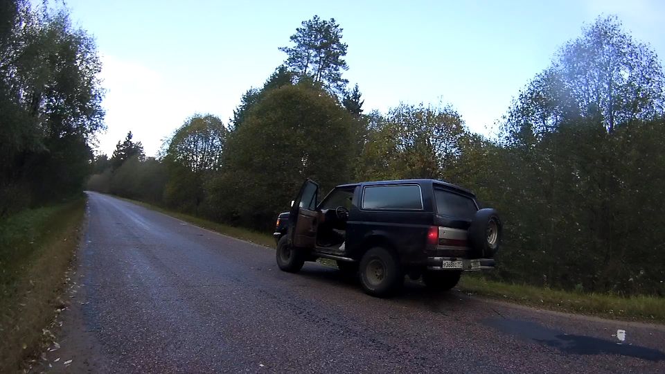 1987 Ford Bronco parked on a wet road with driver's door open.