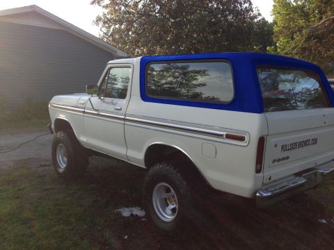 1994 Ford Bronco - A white 1978-1979 Ford Bronco with a blue soft top is parked outdoors on a grassy and muddy area next to a gray building. The vehicle is sh…