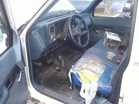 1994 Ford Bronco - The interior of a white pickup truck shows a worn driver's seat with torn upholstery and blue tarp covering. The dashboard and steering whe…