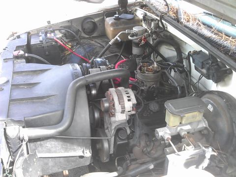 1994 Ford Bronco - The engine bay of a vehicle, showing the radiator fan, alternator, carburetor, and battery. Various hoses and wires are visible throughout…