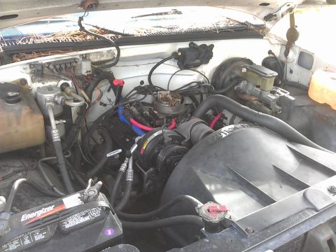 1994 Ford Bronco - A close-up view of the engine bay of a vehicle, showing various components including the battery, engine block, hoses, and wiring.