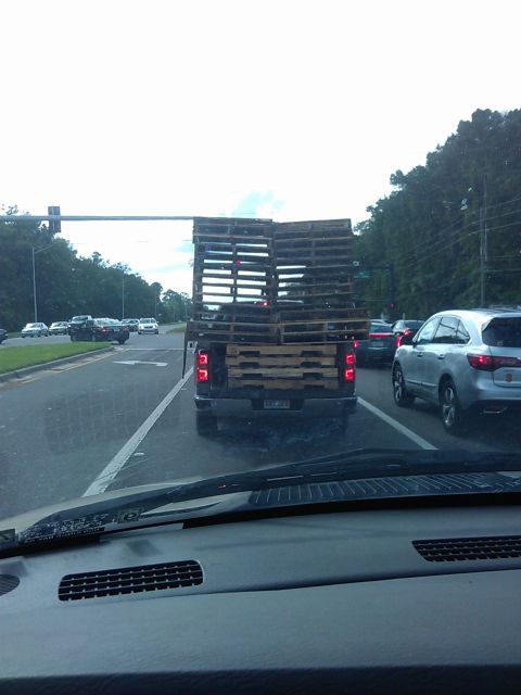 1994 Ford Bronco - The rear of a pickup truck is loaded high with wooden pallets, blocking the view of the bed. The truck is in traffic on a wet road.