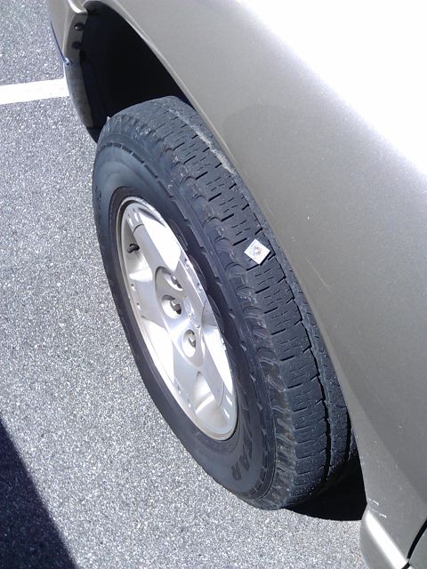 1994 Ford Bronco - A close-up view of a tire on a tan SUV, showing a small, square sticker adhered to the sidewall. The vehicle is parked on an asphalt surfac…