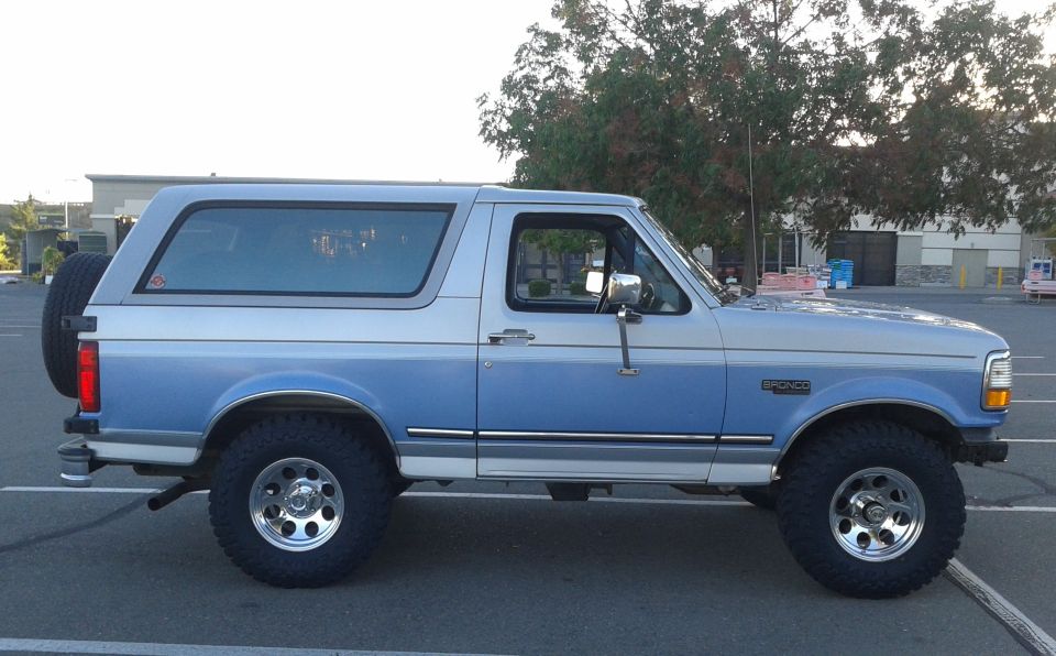 Side view of a blue and silver 1996 Ford Bronco with a spare tire on the back