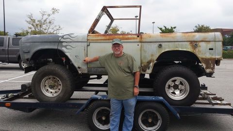 1972 Ford Bronco - A man poses with a weathered Ford Bronco, showing off its classic body style and custom flame paint accents.