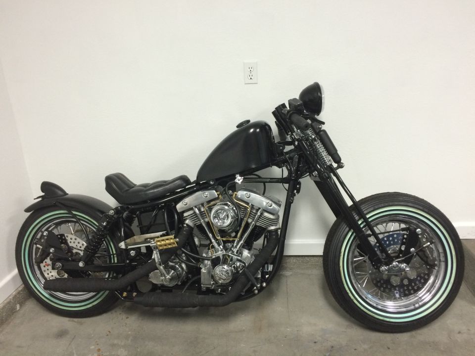 Black custom motorcycle with a V-twin engine, custom tank, and whitewall tires