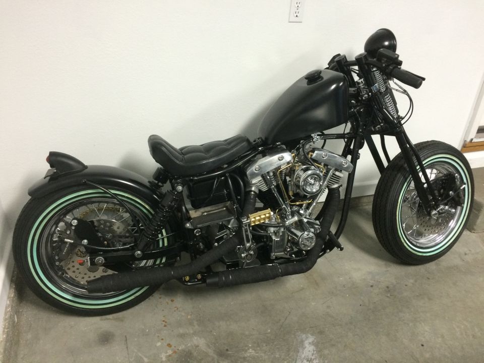 Black custom motorcycle with whitewall tires and exposed engine, viewed from the side