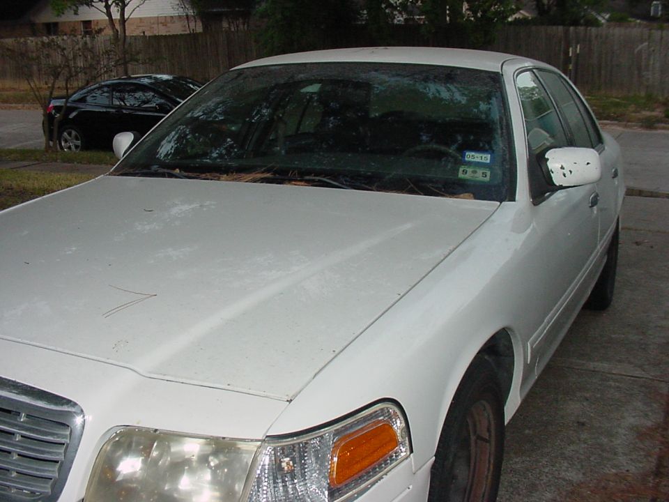 White 2001 Ford Crown Victoria, front quarter view, showing faded paint and a cracked side mirror