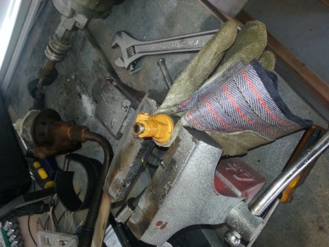 1994 Ford Bronco - A yellow fuel injector is secured in a vise, surrounded by tools, suggesting a repair or maintenance task.