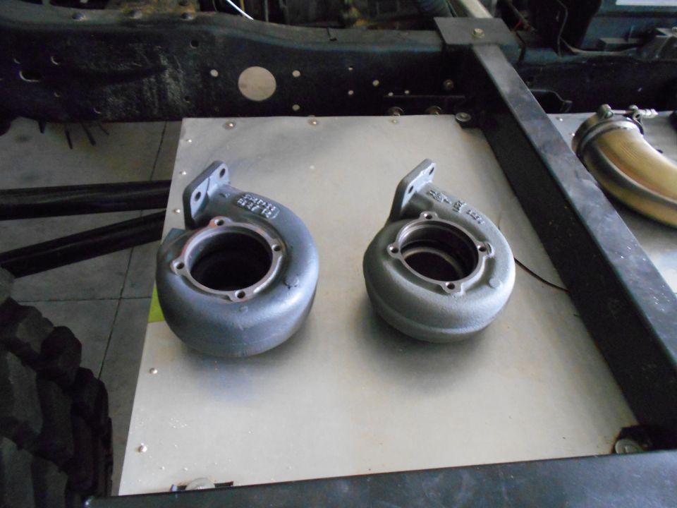 two turbocharger housings on a metal plate, part of a vehicle frame above