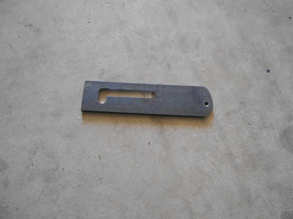 Metal bracket with a rectangular cutout and a rounded end with a hole, lying on a concrete surface