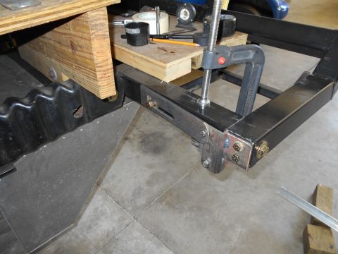 1992 Ford Bronco - A vehicle frame is clamped and supported by wood in this close-up view, with a black corrugated panel visible on the left.