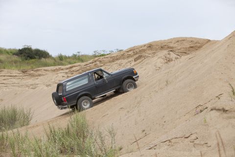 1987 Ford Bronco - Black 1987 Ford Bronco navigates a steep sand dune with a spare tire mounted on the back.