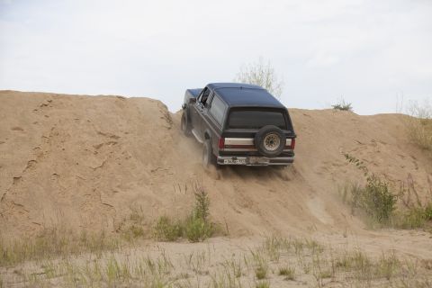 1987 Ford Bronco - A 1987 Ford Bronco navigates a steep sand dune, kicking up dust.
