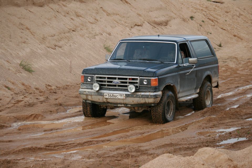 Dark Ford Bronco driving on a muddy dirt road. License plate reads P368BC 197