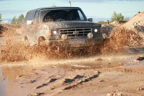 1987 Ford Bronco - This 1987 Ford Bronco navigates a challenging muddy terrain, kicking up a significant spray.