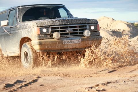 1987 Ford Bronco - Ford Bronco driving through mud splash.