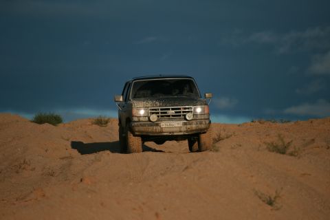 1987 Ford Bronco - A 1987 Ford Bronco navigates sandy terrain under a dramatic sky.