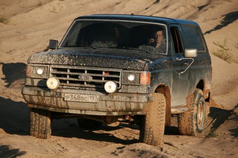1987 Ford Bronco - Mud-covered 1987 Ford Bronco navigates a sandy off-road trail.