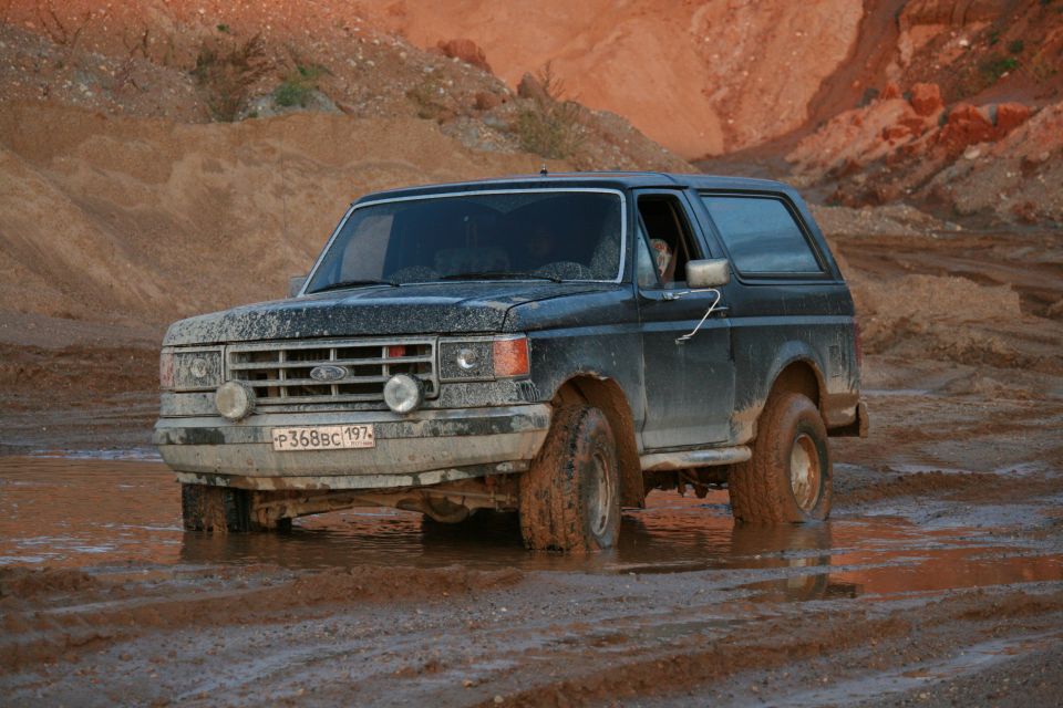 Dark blue 1987 Ford Bronco stuck in mud, front-left tire submerged